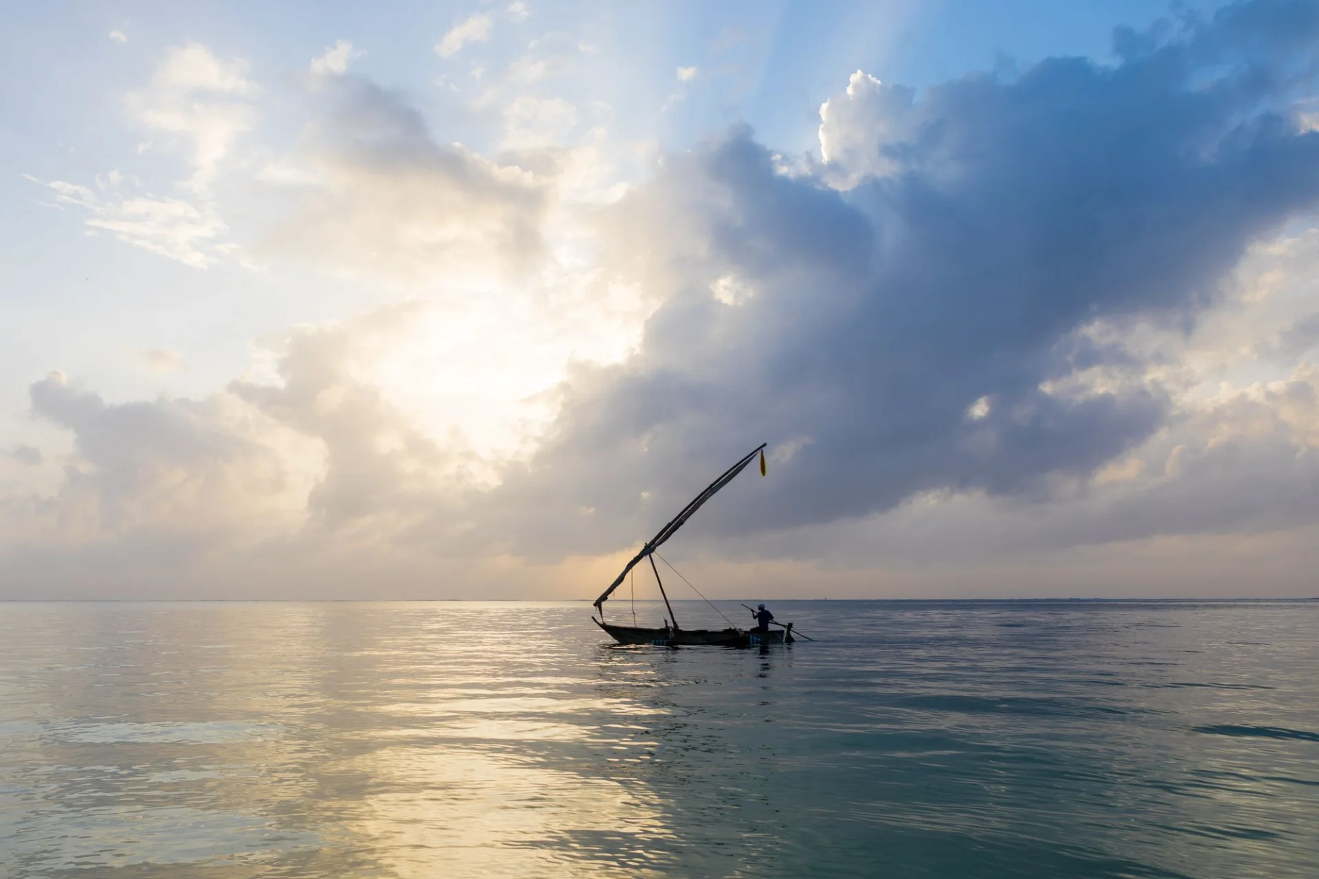 A lone fisherman sailing across calm water at sunrise in Mombasa