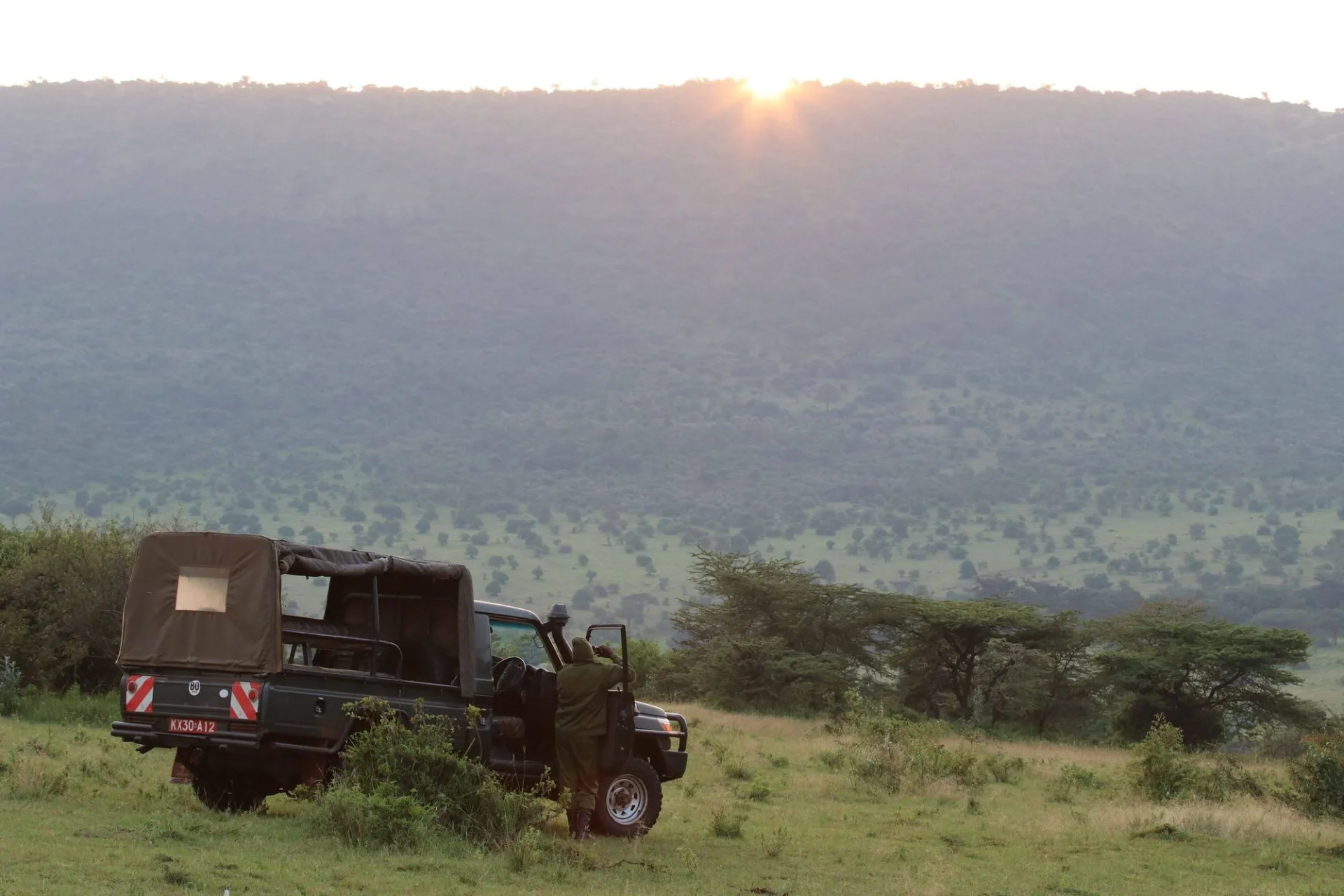 A guide beside a safari vehicle overlooking the hills in Narok, Kenya
